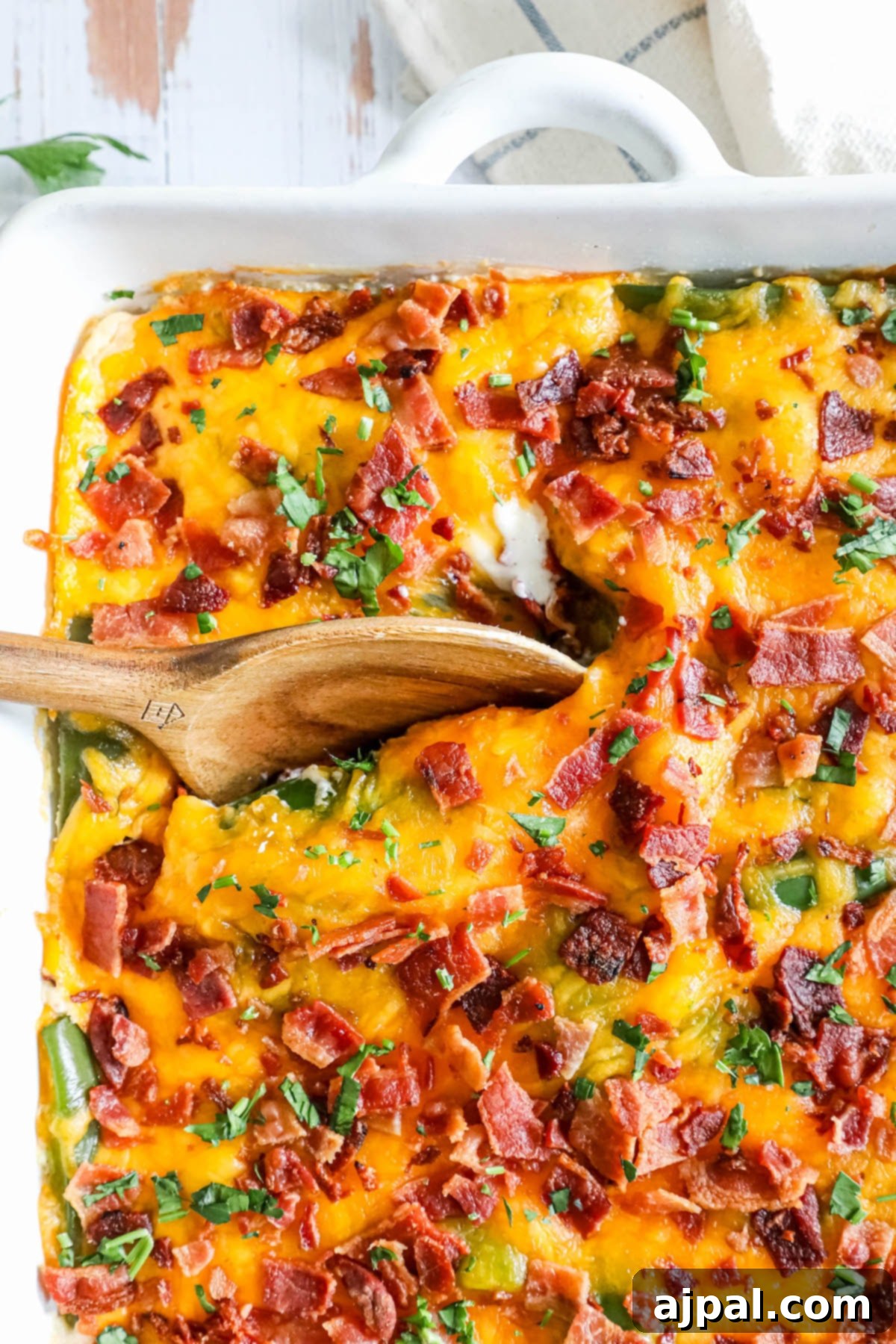 Simple Savory Chicken Bakes 8 A savory casserole made with crispy bacon and tender green beans, stirred with a wooden spoon. The dish features a creamy, spicy filling with chicken and cheese, topped with golden-baked ingredients.