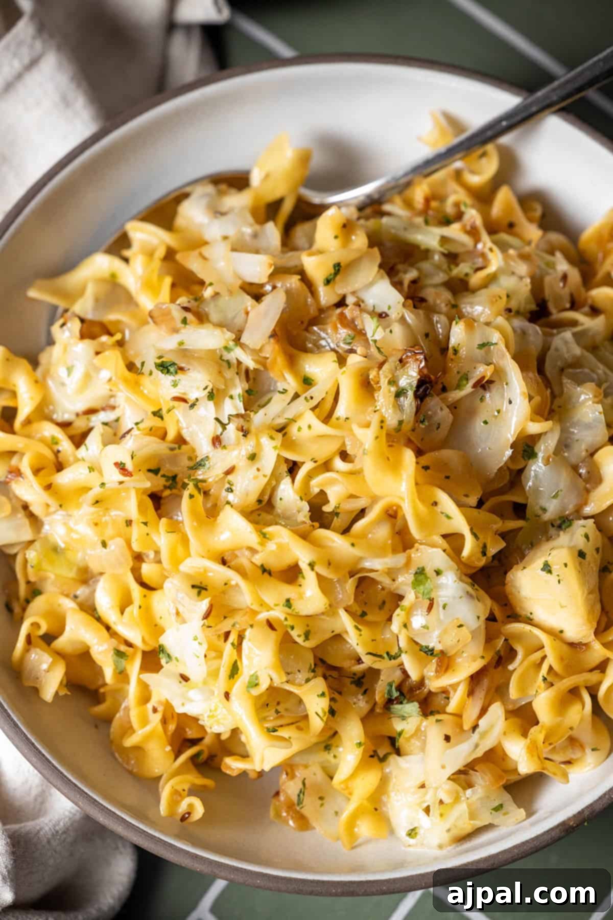 Homestyle Cabbage Noodles 11 A plate of cooked cabbage and noodles mixed with sautéed herbs, with a fork resting on the side of the dish.