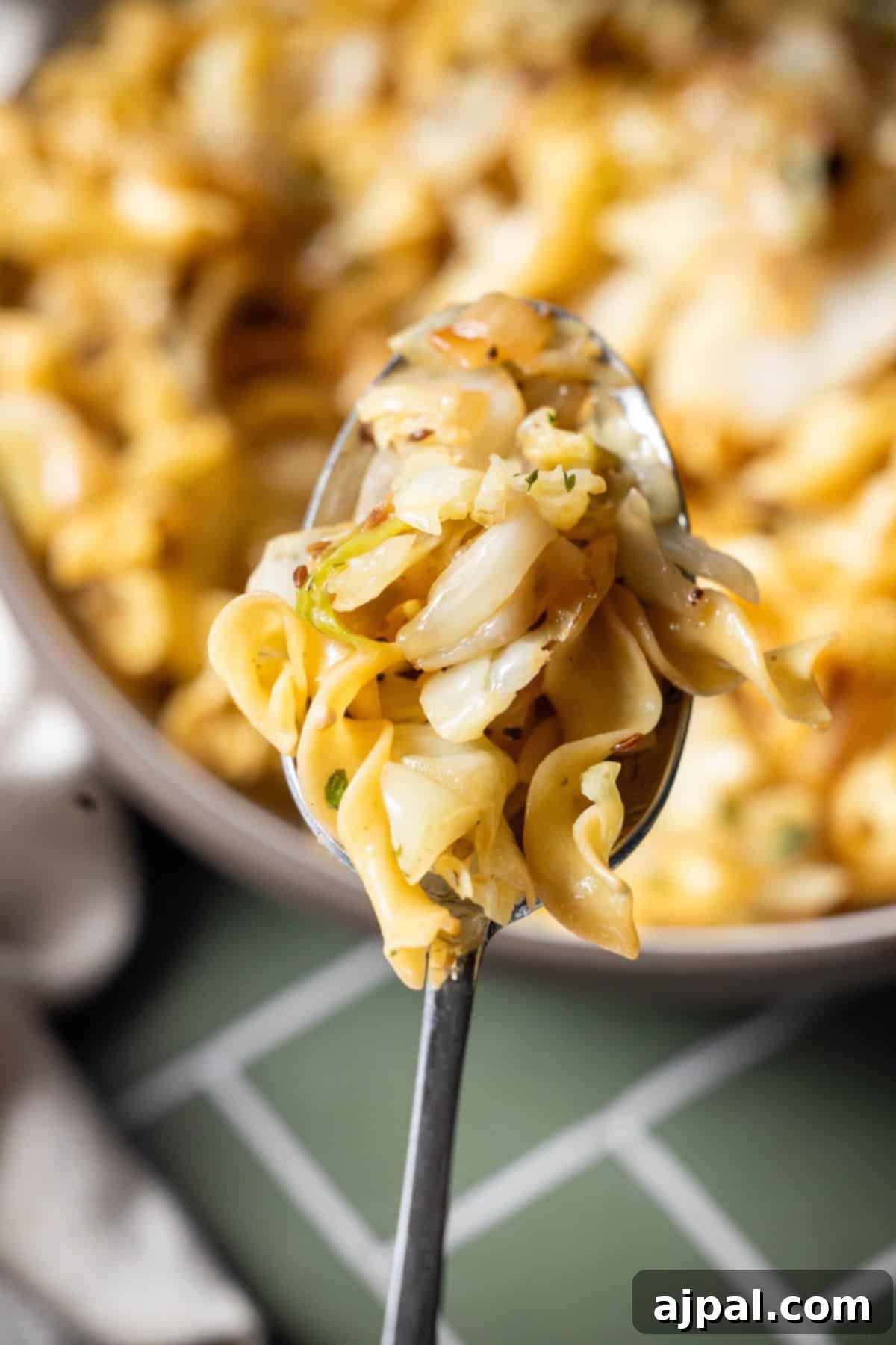 Homestyle Cabbage Noodles 4 A close-up of a spoonful of cooked egg noodles with sautéed cabbage, held above a bowl filled with savory cabbage and noodles.
