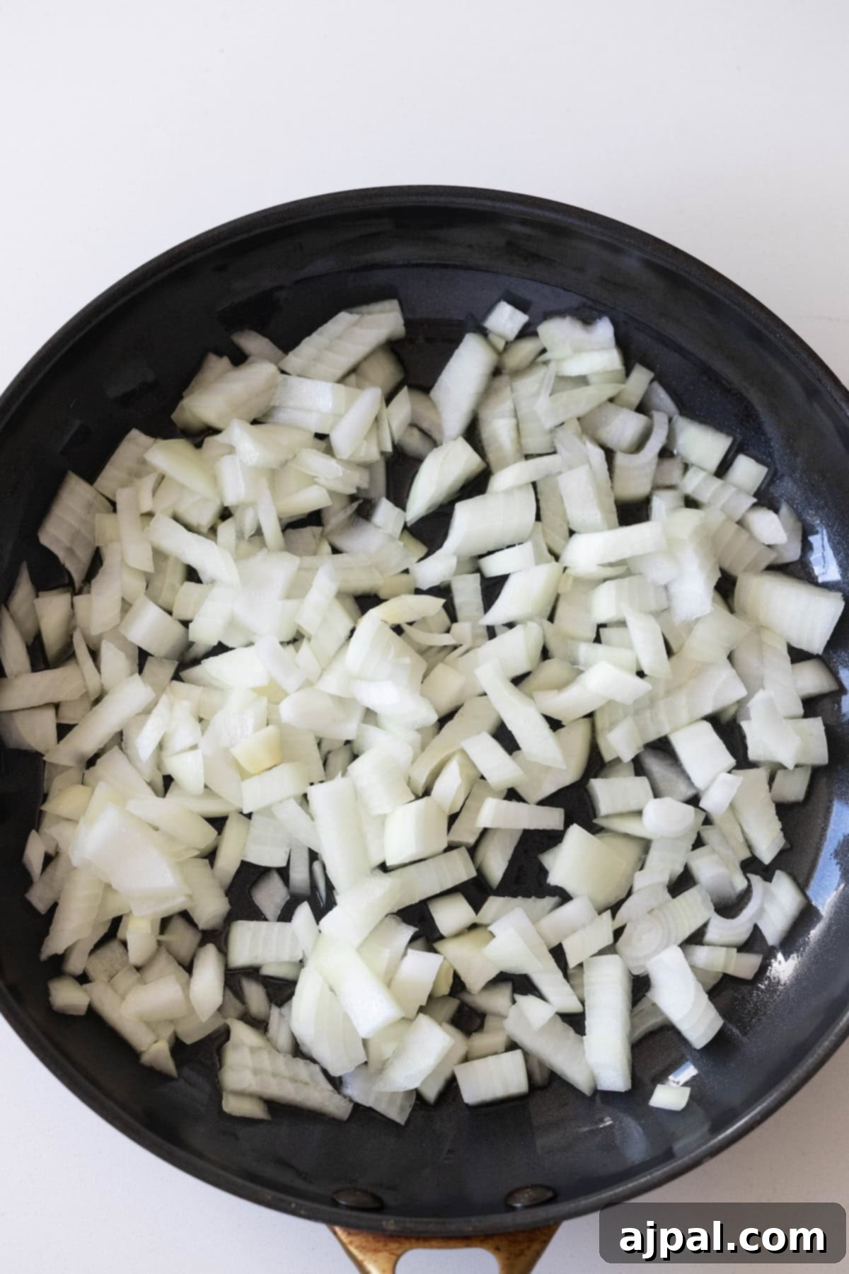 Homestyle Cabbage Noodles 6 A frying pan filled with raw, chopped white onions and cabbage rests on a white surface, ready to be mixed with noodles.