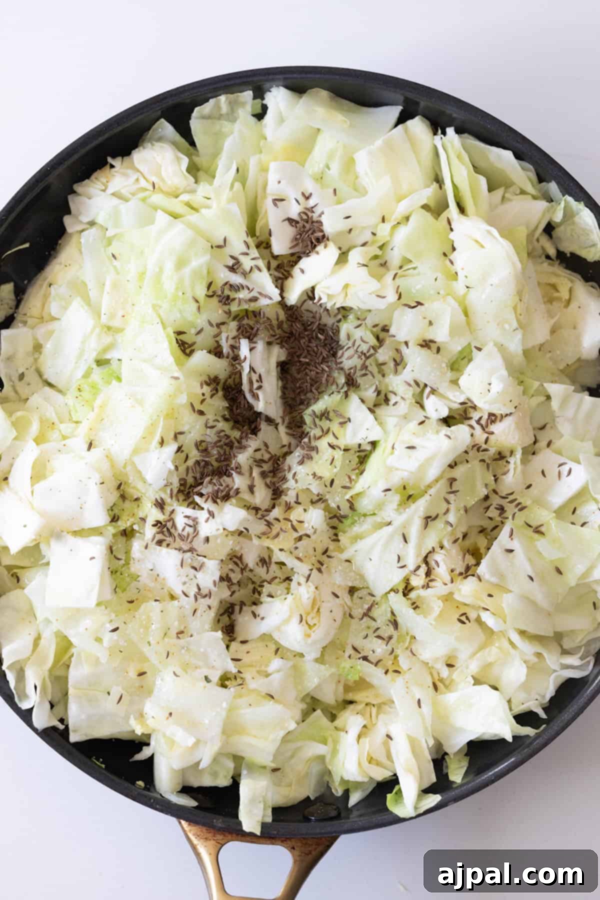 Homestyle Cabbage Noodles 8 Chopped cabbage with caraway seeds and pepper in a black skillet, perfect for creating delicious Cabbage and Noodles.