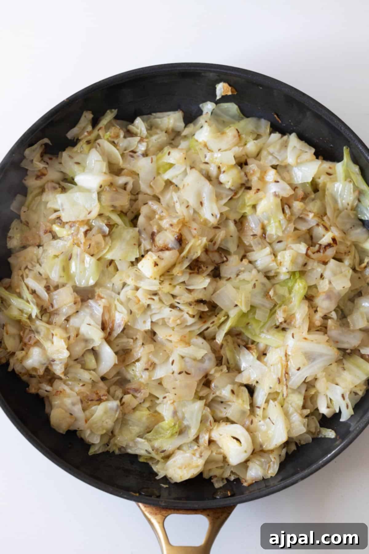 Homestyle Cabbage Noodles 9 A black skillet filled with sautéed chopped cabbage and noodles, showing browned edges, rests on a white surface.