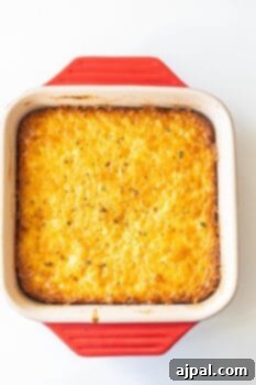 A golden-brown baked corn pudding casserole in a red and white ceramic dish, freshly out of the oven, highlighting its creamy texture and savory appeal.