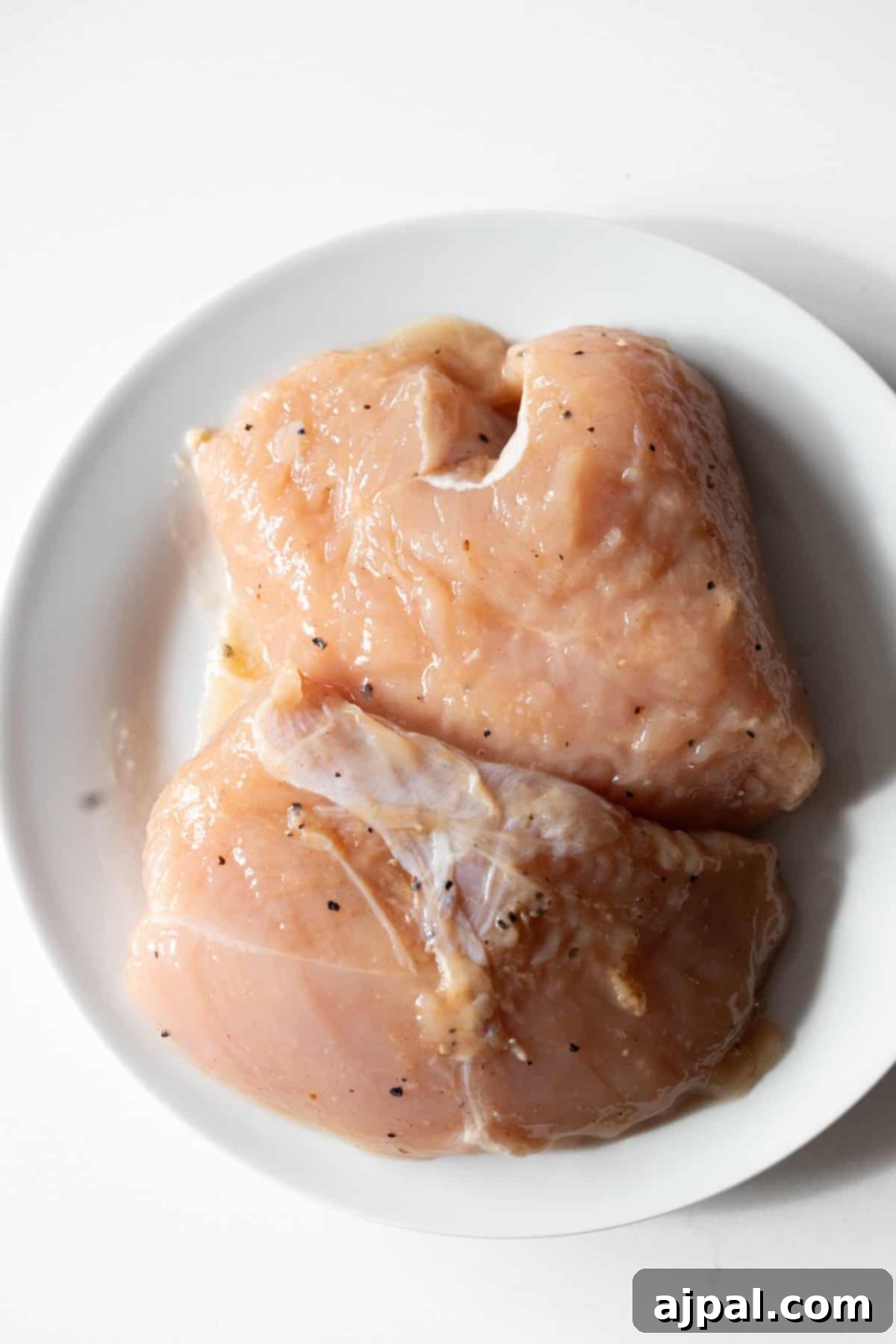 Two raw, seasoned turkey tenderloins on a white plate.
