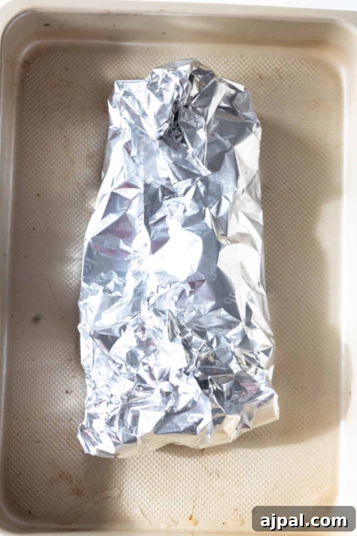 A baking tray with turkey tenderloin wrapped in foil.
