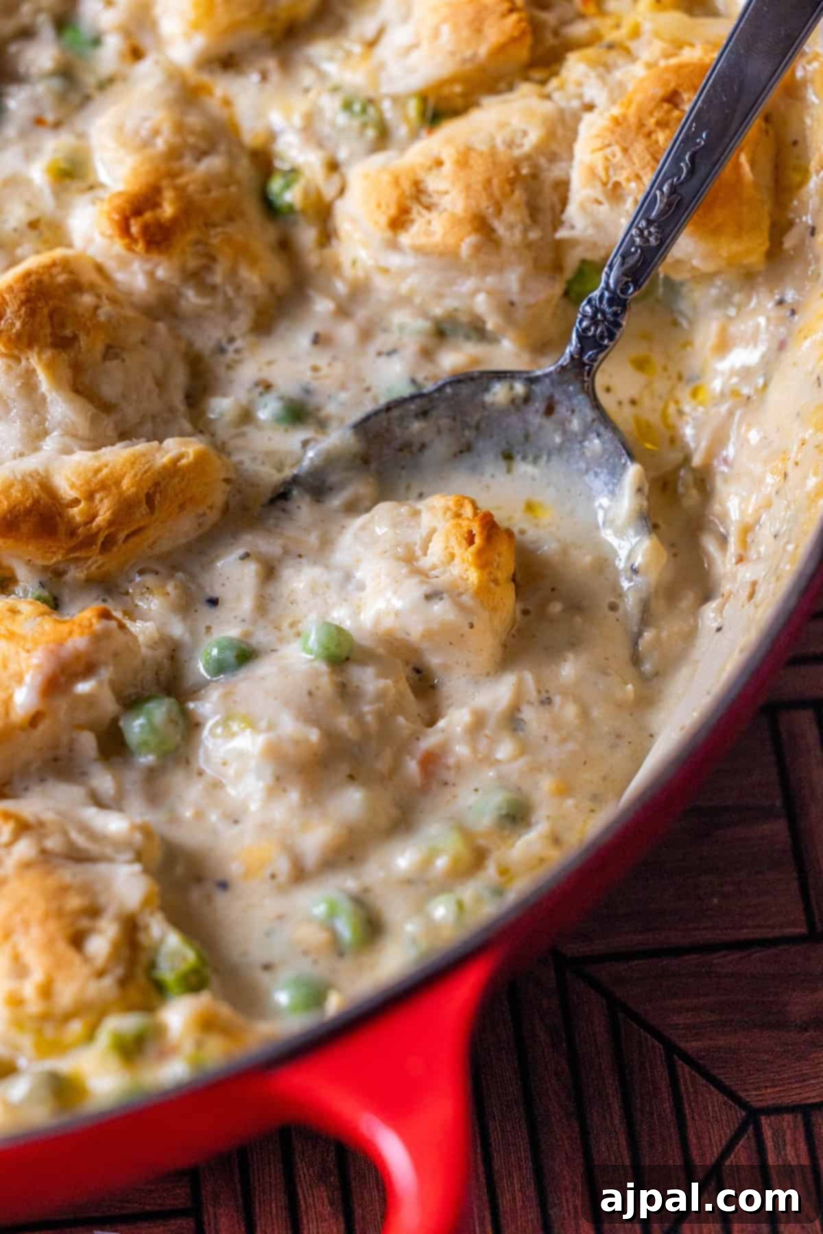 Creamy turkey casserole with biscuits and peas being scooped from a red baking dish.