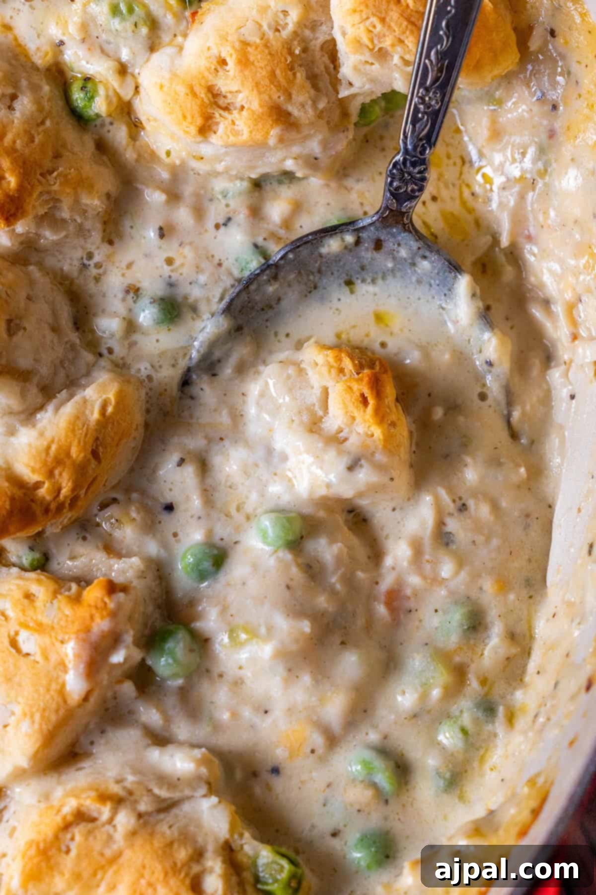 Spoonful of creamy biscuit casserole featuring tender turkey and vegetables, with peas and a golden topping.