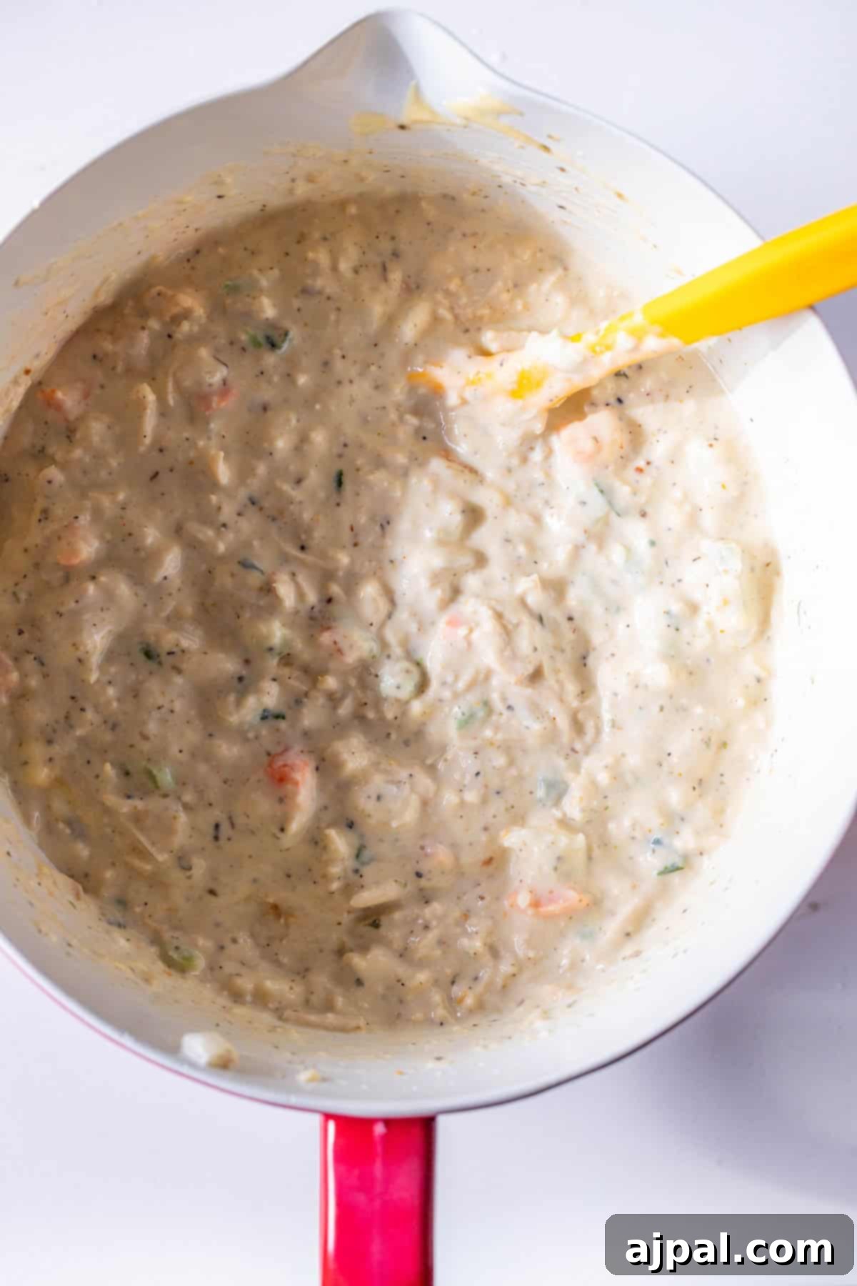 Thick, creamy soup with vegetables and leftover turkey being stirred with a yellow spatula.