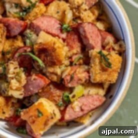 A bowl of sausage and bread stuffing with herbs and chopped vegetables, featuring browned bread cubes and hearty slices of Polish Kielbasa.