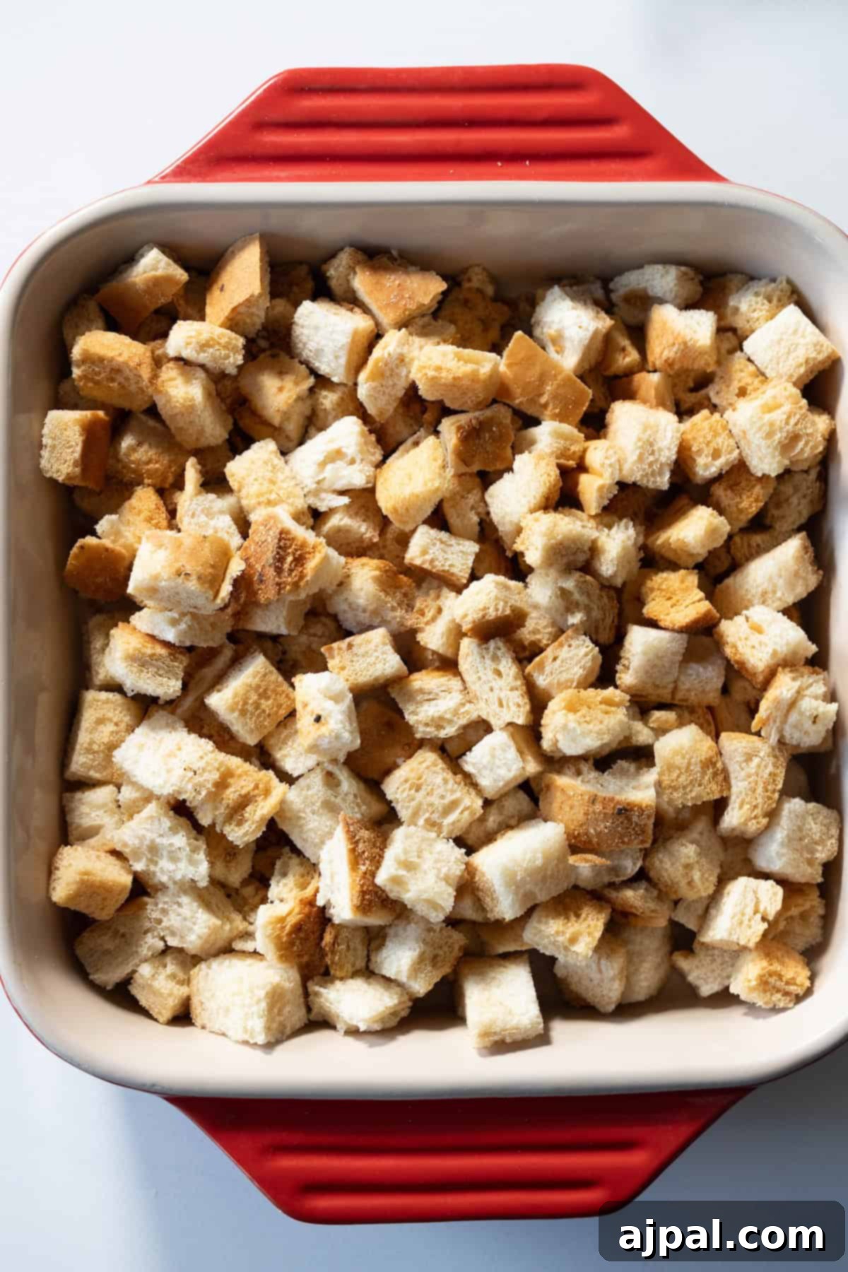 A baking dish filled with perfectly cut bread cubes for stuffing, showcasing a delightful mix of white and brown pieces, beautifully arranged on a pristine white surface.