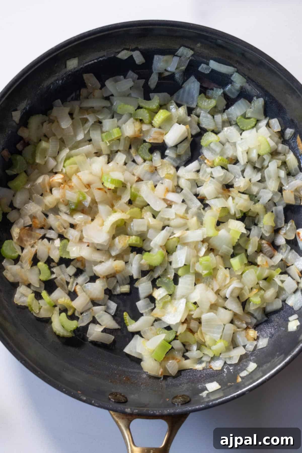 Diced onions and celery expertly sautéed in a black skillet, showcasing the perfect browning and softening—laying the foundation for the savory Kielbasa stuffing.