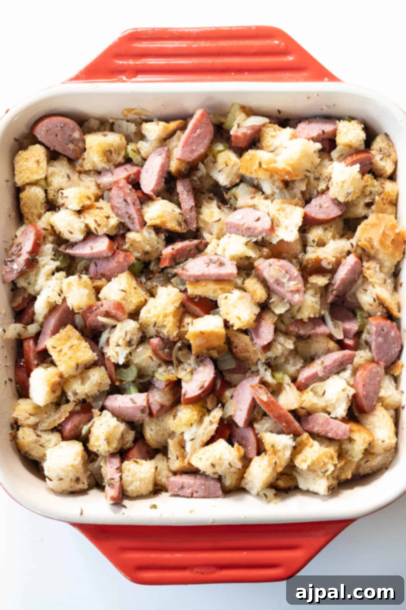 A square red baking dish filled with a tantalizing mixture of cubed bread and sliced Polish Kielbasa, baked together to create a savory and satisfying stuffing.
