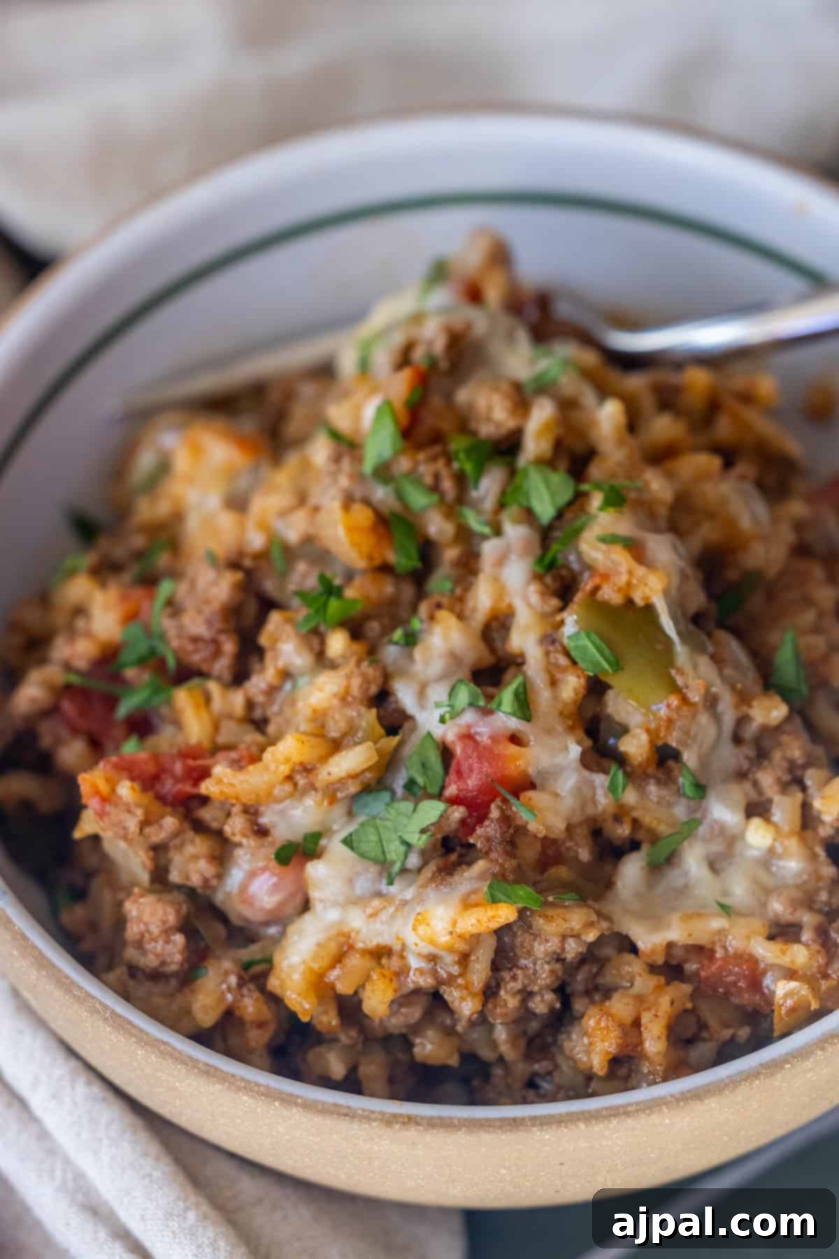 Fiery One-Pot Taco Skillet 3 Bowl of cheesy ground beef and rice casserole, inspired by a One Pot Spicy Taco Rice Skillet, topped with chopped parsley and served with a fork.