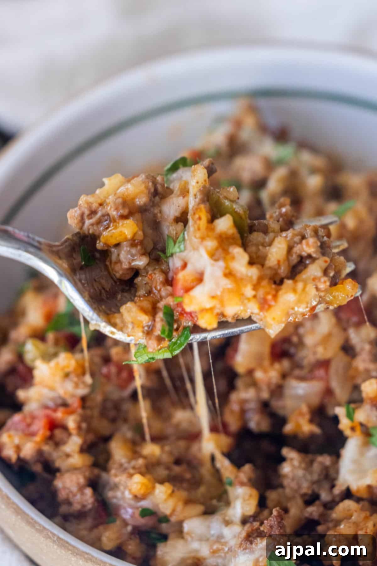 Fiery One-Pot Taco Skillet 4 A close-up of a spoonful of cheesy ground beef casserole with rice, vegetables, and herbs—just like an easy taco and rice skillet dinner—held above a bowl of the same comforting dish.