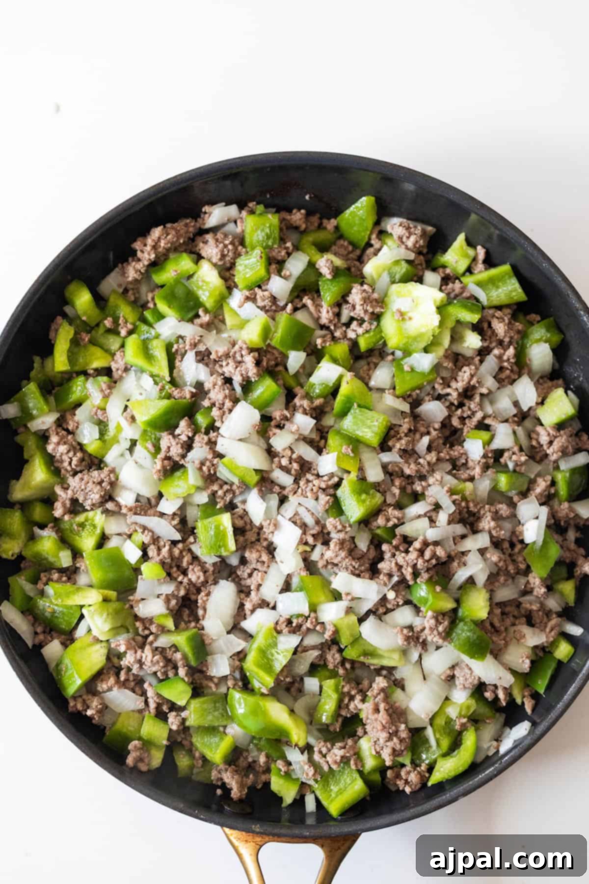 Fiery One-Pot Taco Skillet 6 A skillet filled with cooked ground beef, chopped green bell peppers, and diced onions—perfect for an easy taco and rice skillet dinner—set against a white background.