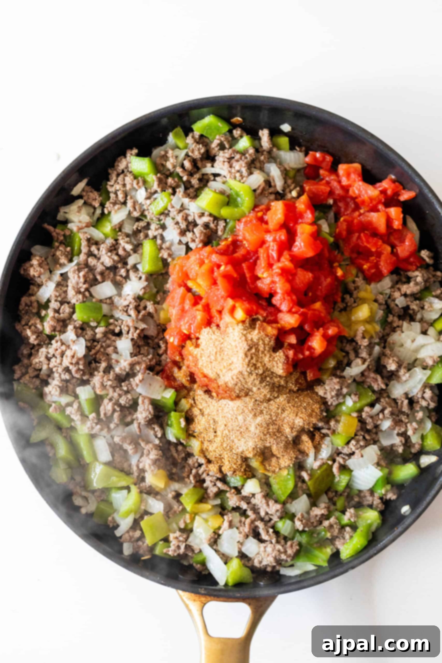 Fiery One-Pot Taco Skillet 7 A skillet filled with cooked ground beef, chopped green bell peppers, onions, canned diced tomatoes, taco seasoning, and rice makes this One Pot Spicy Taco Rice Skillet a flavorful dinner option.