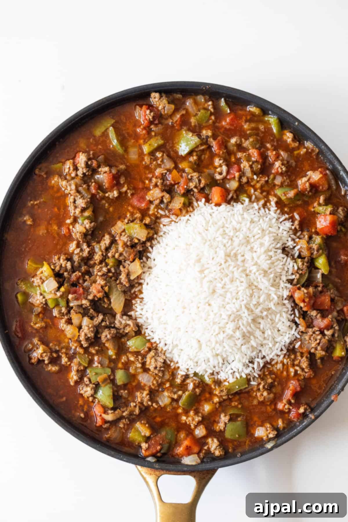 Fiery One-Pot Taco Skillet 8 A skillet filled with ground beef, tomatoes, diced vegetables, and a mound of uncooked white rice on top—ready to be mixed for an easy taco and rice skillet dinner.