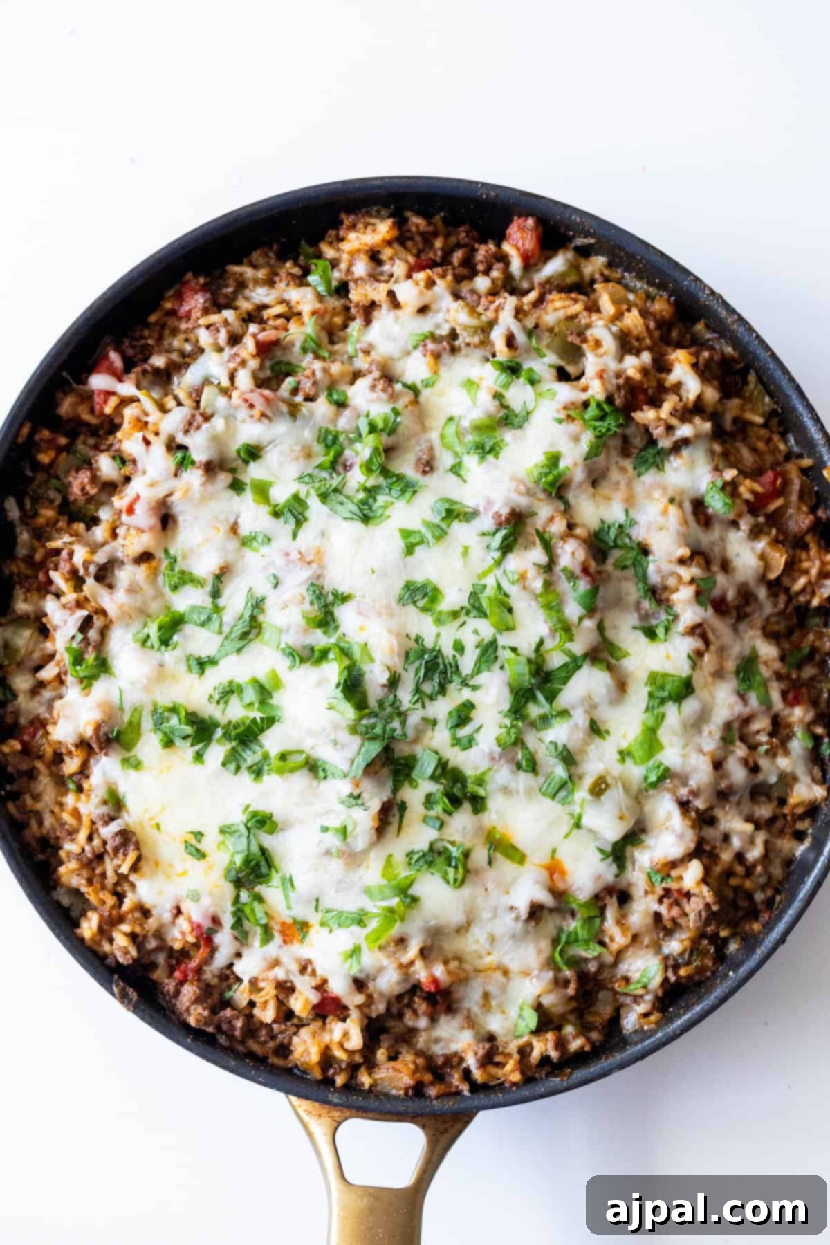 Fiery One-Pot Taco Skillet 10 A skillet filled with ground meat, rice, tomato, melted cheese, and chopped green herbs on top—this One Pot Spicy Taco Rice Skillet is photographed from above.