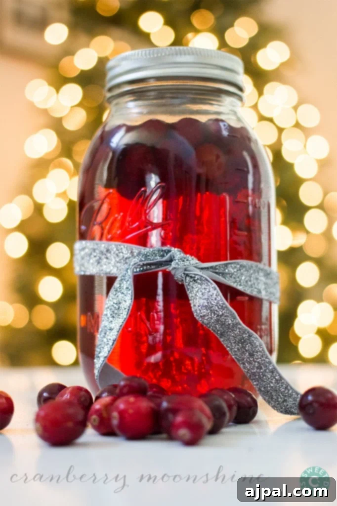 A mason jar overflowing with sparkling cranberry moonshine, adorned with fresh cranberries and festive lights softly blurred in the background, signaling a joyful holiday season.