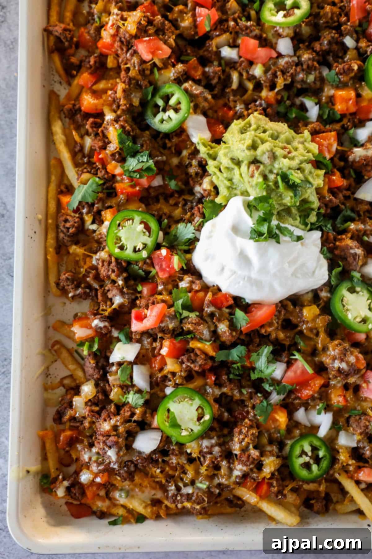 Try our French Fry Nachos: a tray of crispy fries topped with ground beef, melted cheese, diced tomatoes, onions, jalapeños, cilantro, guacamole, and sour cream—a deliciously easy nacho loaded fries recipe you'll love!.