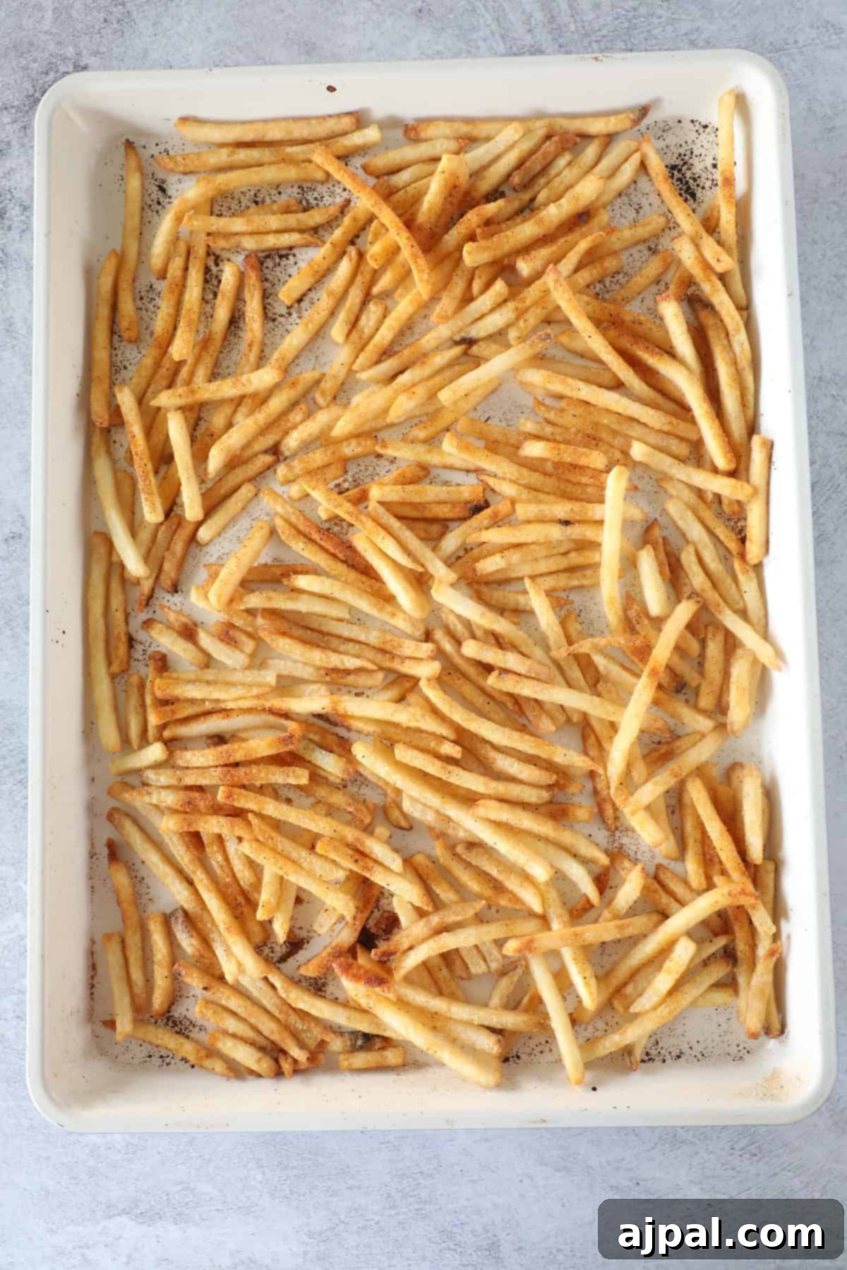 A baking sheet filled with evenly spread, seasoned French fries on a light gray surface—perfect for trying an Easy Nacho Fries twist or your favorite French Fry Nachos recipe.