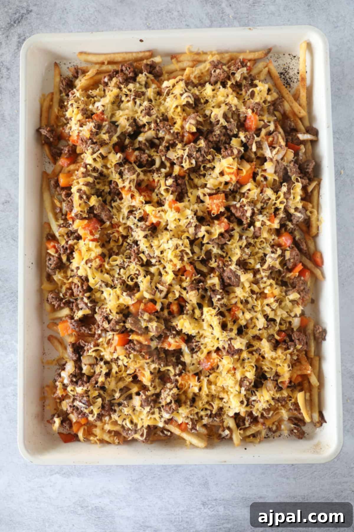 A baking dish filled with a layered casserole made of cooked ground beef, pasta, diced carrots, and melted cheese on top—like an Easy Nacho Fries twist in casserole form.