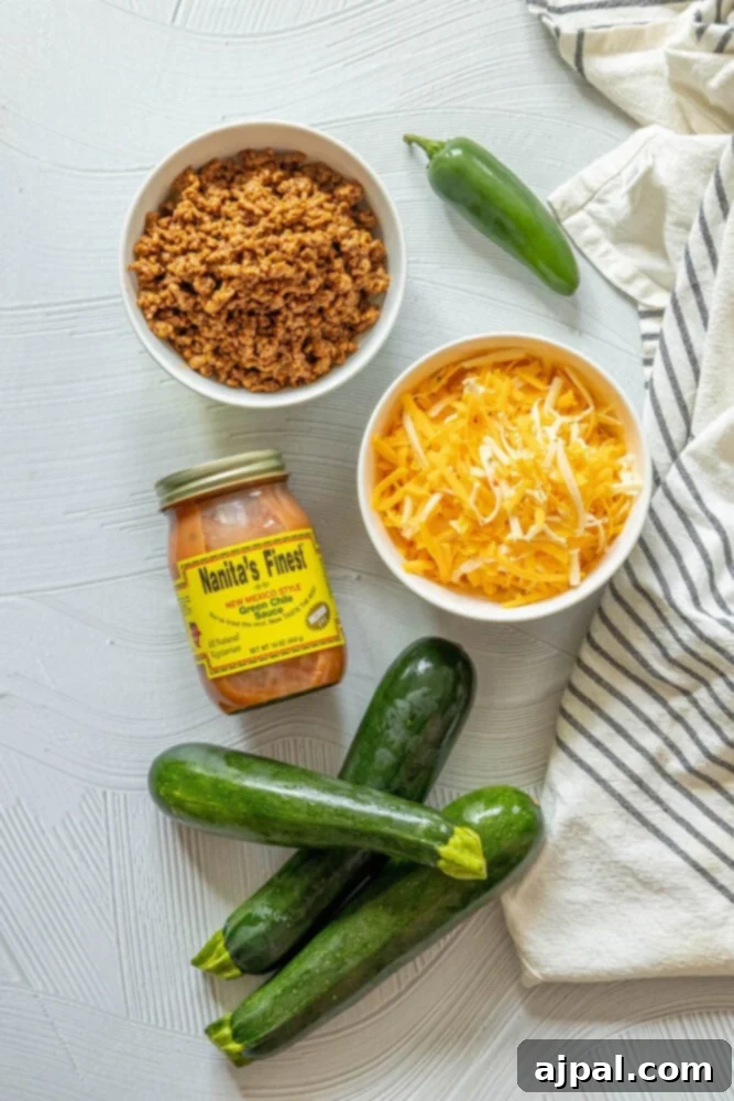 Loaded Zucchini Boats 5 A vibrant selection of ingredients on a table, including fresh jalapeños, whole zucchinis, a bowl of green chile enchilada sauce, cooked ground beef taco mixture, and a pile of shredded cheese.
