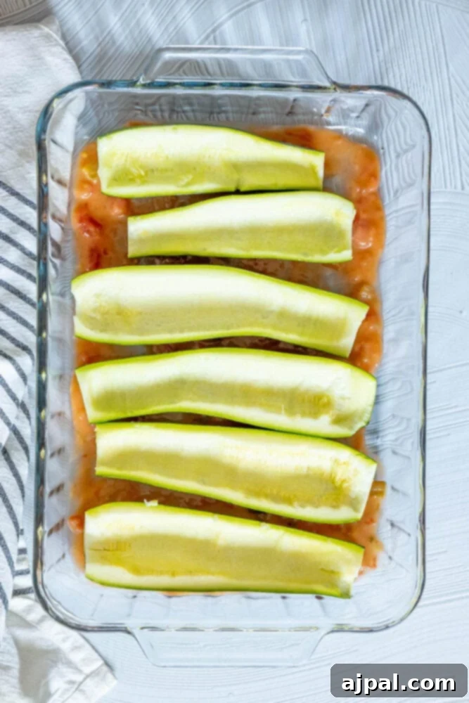 Loaded Zucchini Boats 8 Halved and cored zucchinis nestled in a glass baking dish, already coated with a vibrant green enchilada sauce, awaiting their flavorful filling.