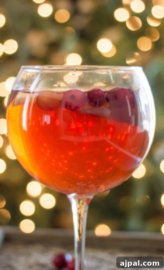 A beautifully garnished glass of Cranberry Apple Sangria with fresh cranberries and apple slices, set against a festive holiday backdrop.