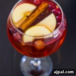 A glass of cranberry apple punch with cinnamon sticks and apples.