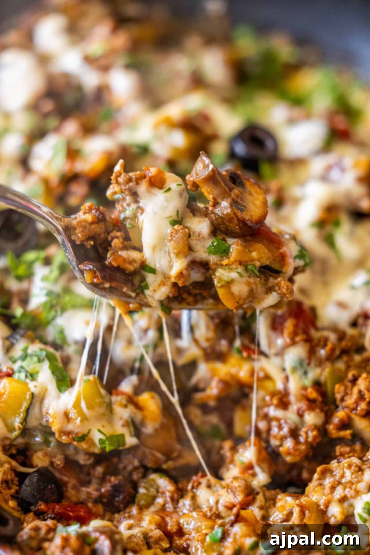 Loaded Cheesy Taco Skillet 11 A close-up of a fork lifting a cheesy, cooked ground meat mixture with vegetables and herbs from a Cheesy Taco Skillet.