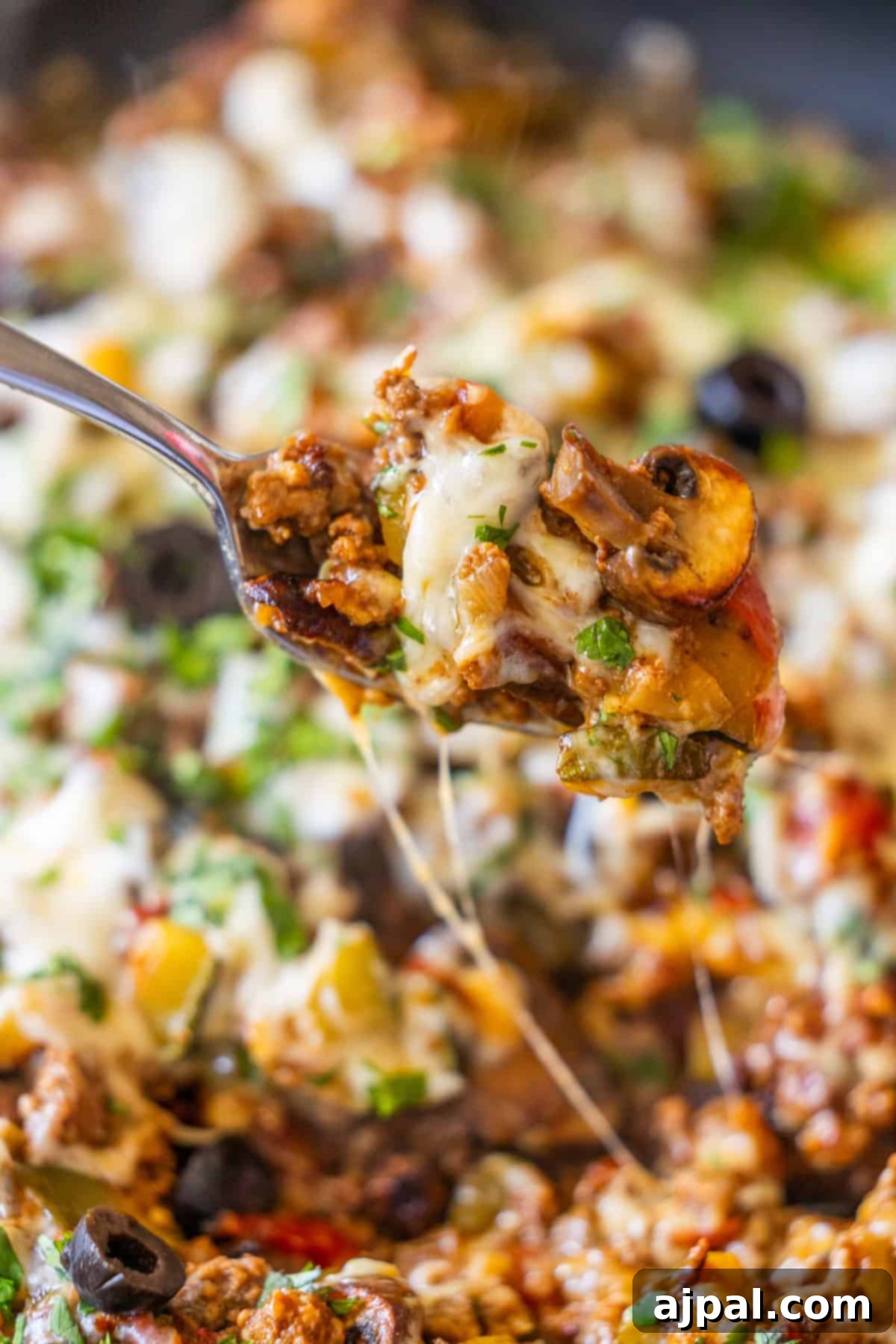 Loaded Cheesy Taco Skillet 14 A close-up of a spoon lifting a cheesy, baked mixture of ground meat, mushrooms, olives, and herbs from a casserole dish—perfect for making The Best Taco Skillet.