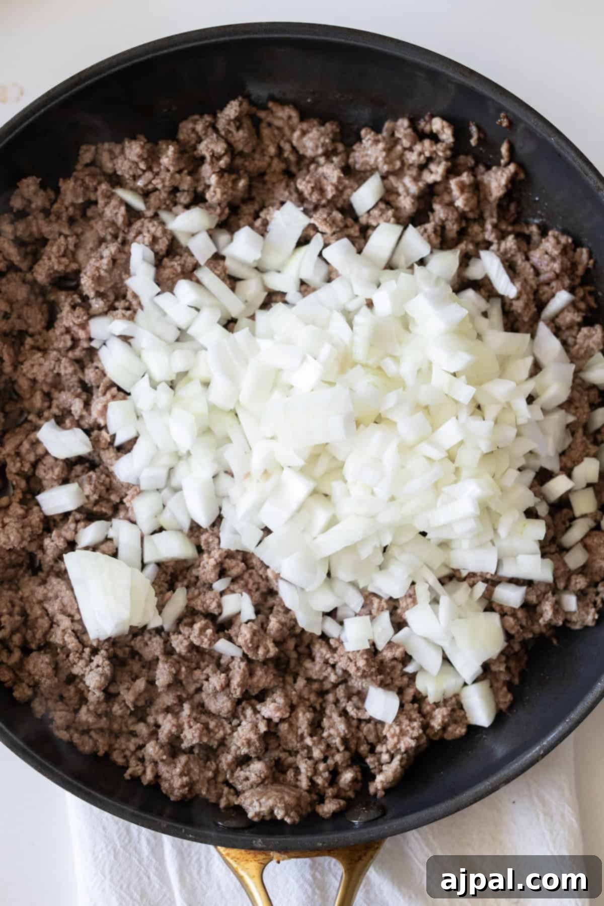 Loaded Cheesy Taco Skillet 5 Ground beef cooking in a skillet with chopped white onions on top, perfect for building a flavorful Cheesy Beef Taco Skillet.