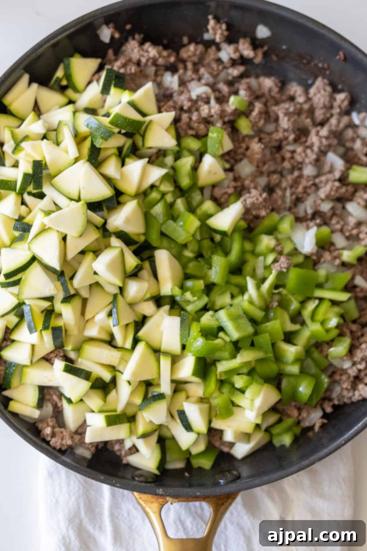 Loaded Cheesy Taco Skillet 6 A skillet filled with cooked ground beef and onions on one side, and raw chopped zucchini and green bell peppers on the other, ready to become a Cheesy Beef Taco Skillet.