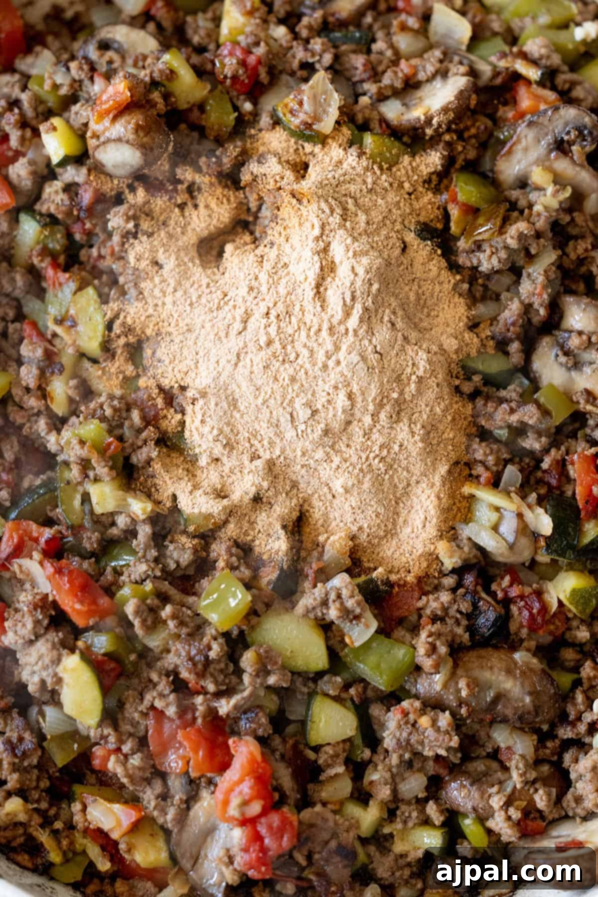 Loaded Cheesy Taco Skillet 8 Ground beef, chopped vegetables, and a mound of taco seasoning mix in a pan, ready to be stirred and transformed into the Best Taco Skillet for a flavorful meal.