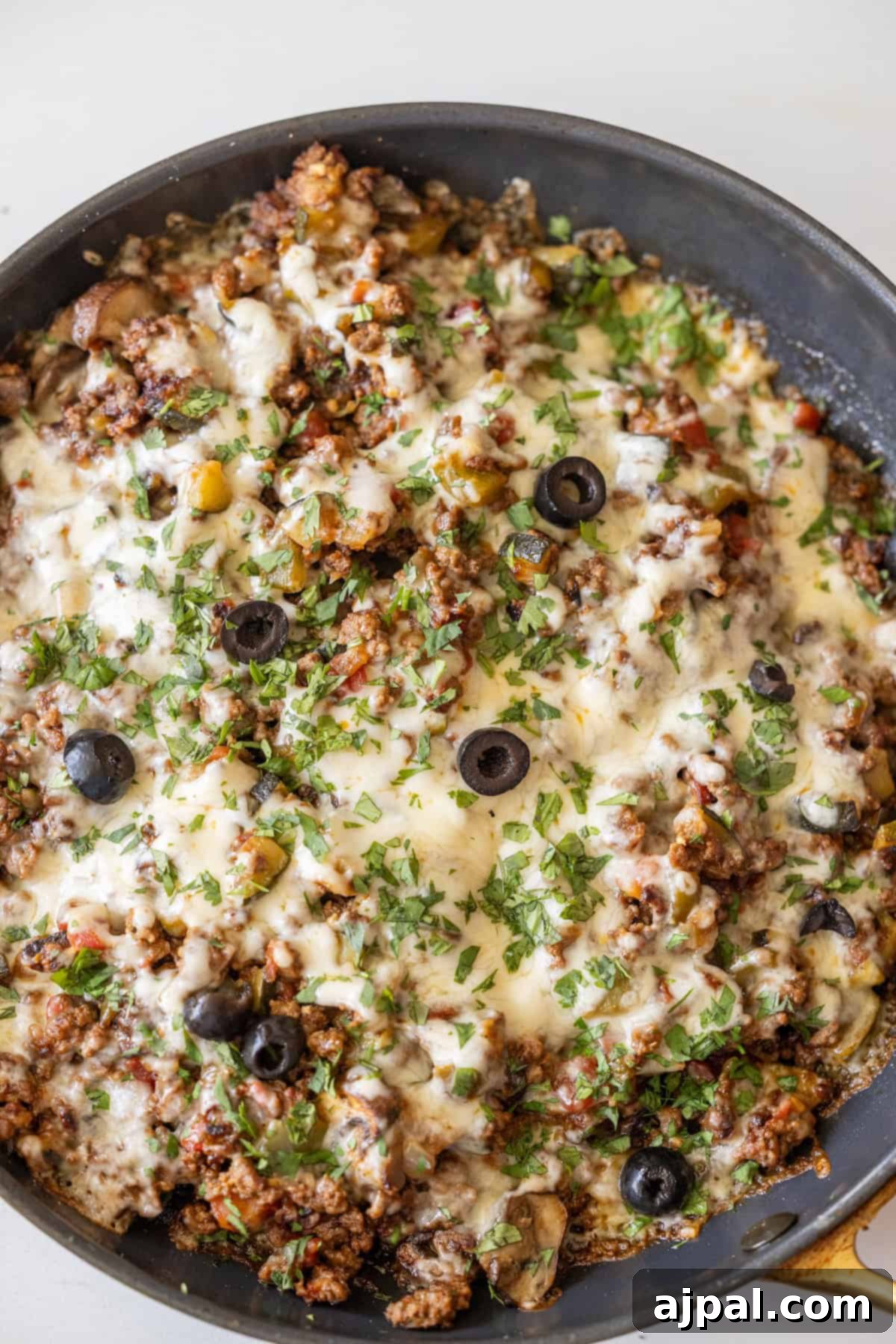 Loaded Cheesy Taco Skillet 10 A Cheesy Taco Skillet filled with cooked ground meat, melted cheese, chopped herbs, black olive slices, and diced vegetables.
