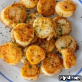 A plate of Perfect Pan Seared Scallops garnished with chopped herbs and seasonings, served on a white dish with a blue trim.