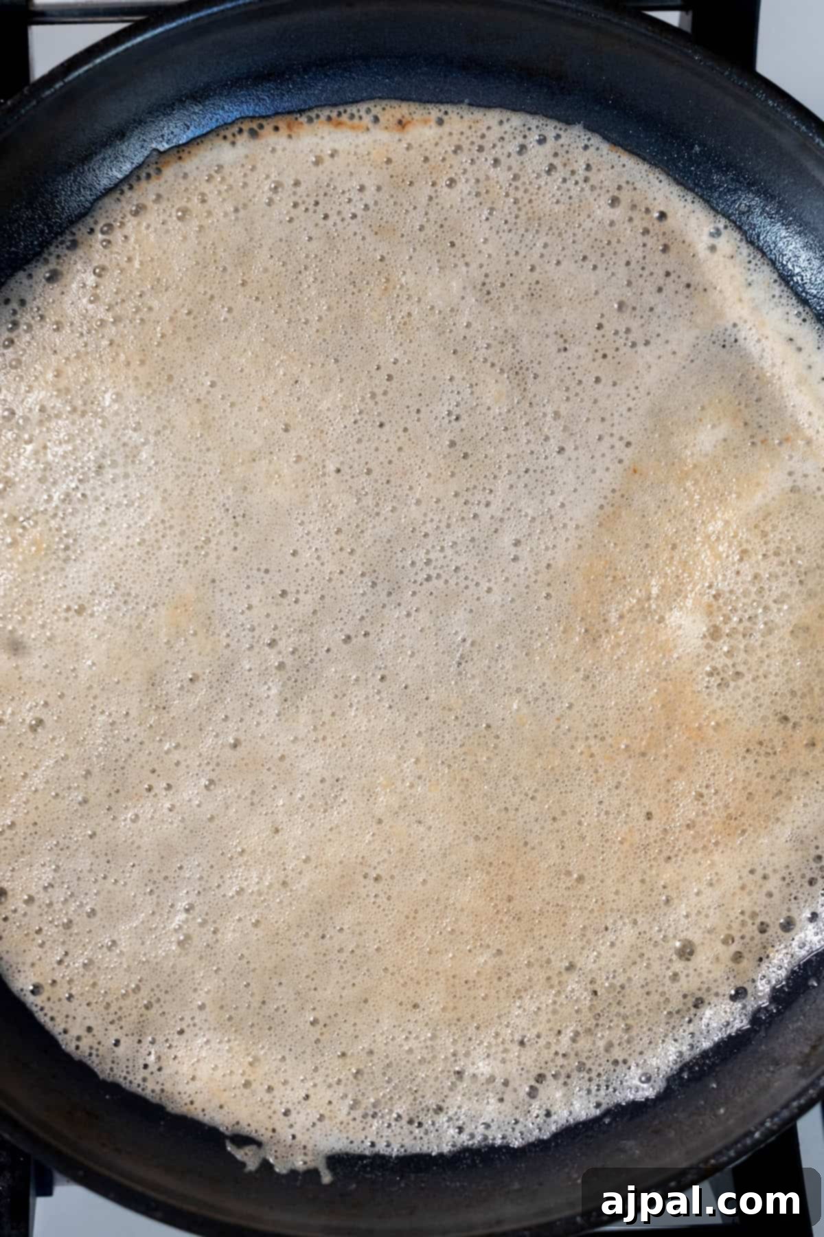 Caramelized Pan Seared Scallops 6 A thin crepe is cooking in a black frying pan on a stovetop, perfect for making sweet treats—or even as a savory base for perfect pan seared scallops.