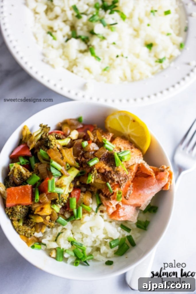 Paleo Salmon Taco Power Bowls 5 A vibrant bowl of salmon and vegetables served on a pristine bed of cauliflower rice, garnished with fresh herbs and a lemon slice.