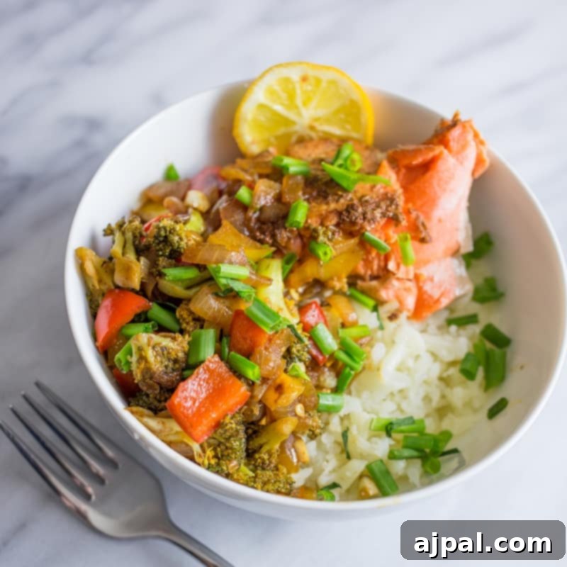 Paleo Salmon Taco Power Bowls 4 A perfectly portioned bowl with fluffy cauliflower rice, seasoned salmon, vibrant broccoli florets, and a sprinkle of fresh chives, garnished with a lemon slice, highlighting a healthy and delicious meal.
