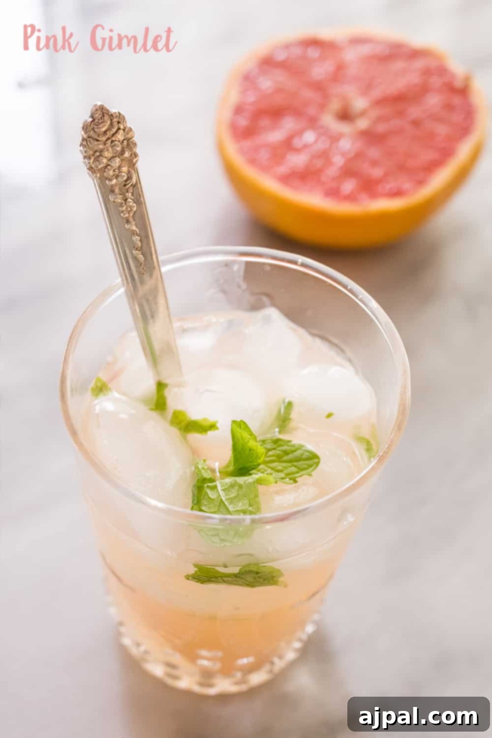 A vibrant pink gimlet cocktail with mint and ice, featuring fresh grapefruit in the background, perfect for a refreshing summertime drink.