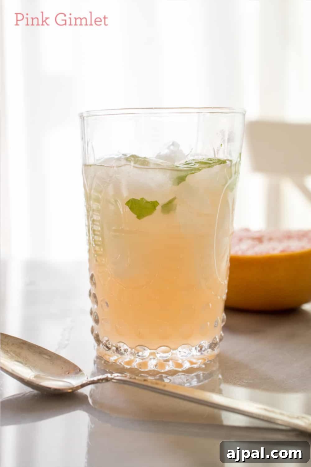 A refreshing pink gimlet cocktail garnished with mint and ice, with grapefruit slices in the background.