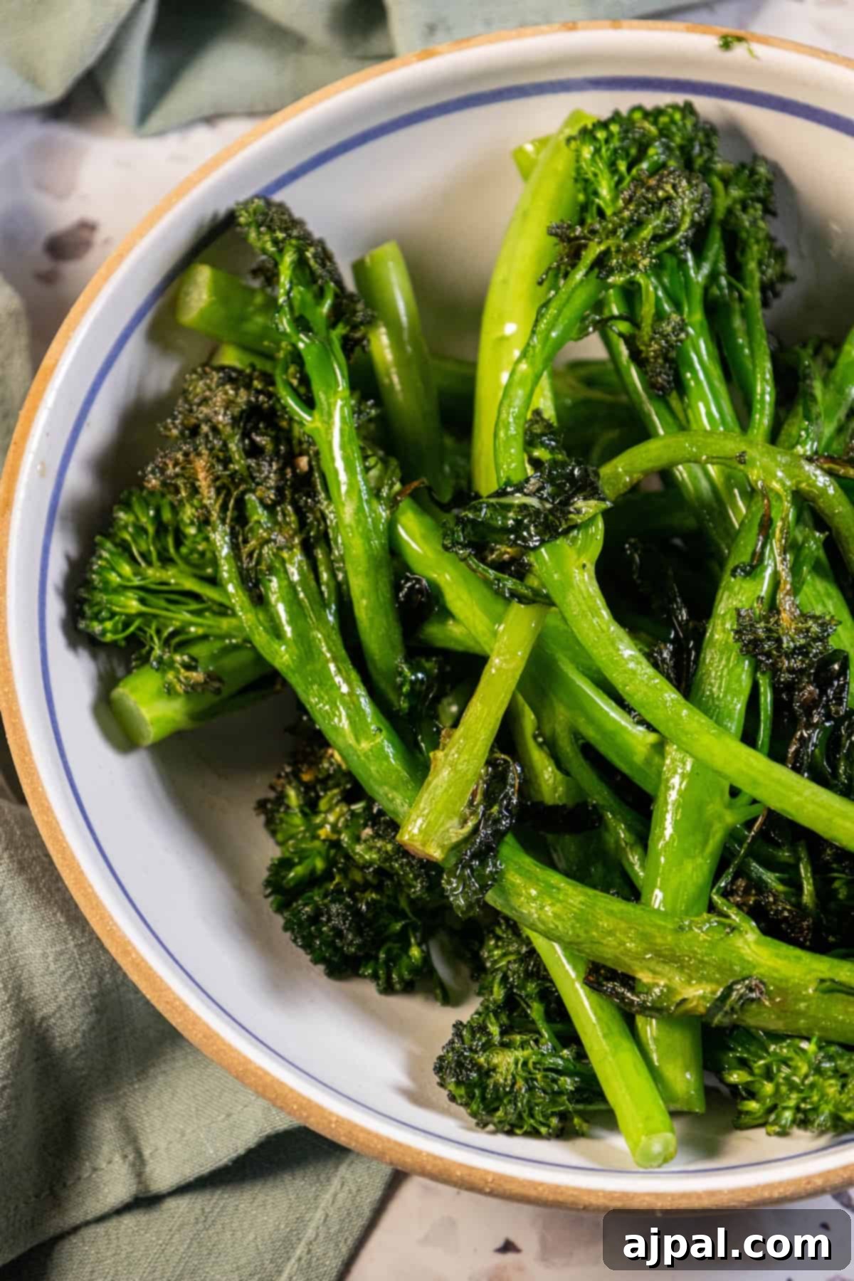 A bowl of sauteed broccolini on a table with a napkin, ready to be served.