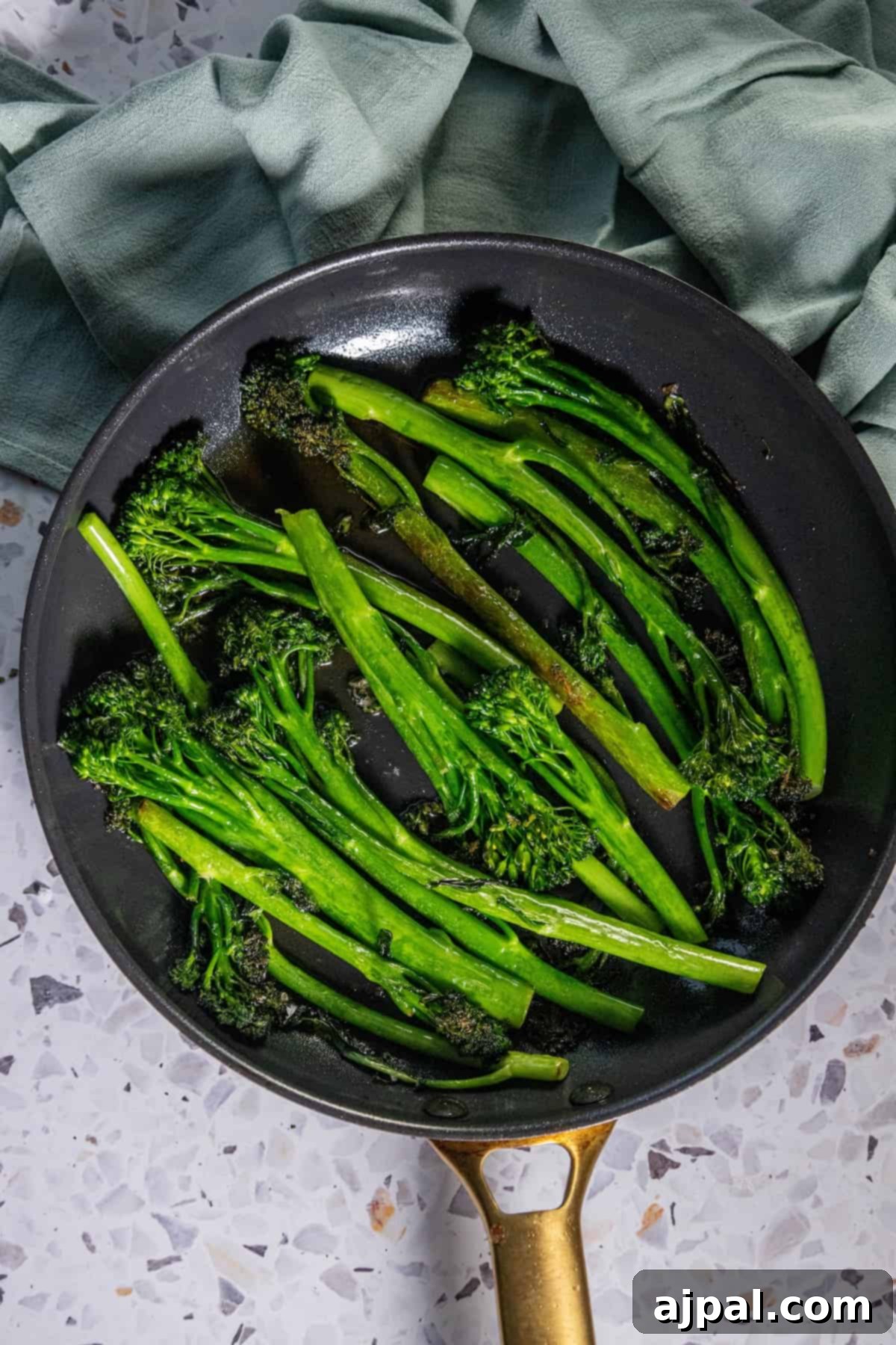 Pan fried broccolini on a table, glistening with butter and seasonings.