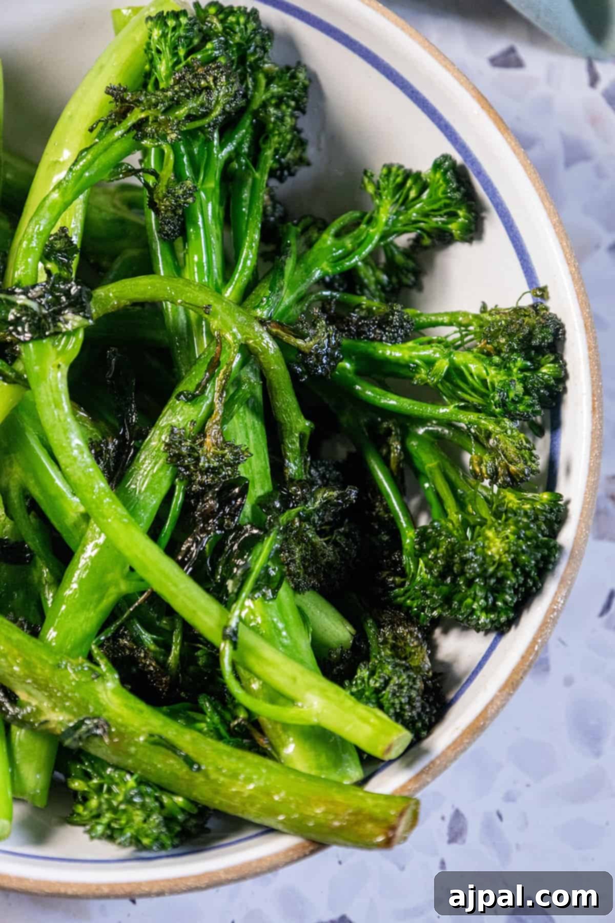A bowl of sautéed broccolini on a table with a napkin, showcasing its delicious appeal.