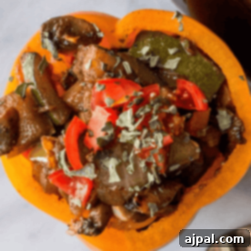 Spicy vegan stuffed bell pepper with diced tomatoes, mushrooms, and herbs on top, served on a white plate.