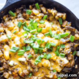A cast iron skillet sizzles with cheesy veggie home fries, a delightful potato dish crowned with chopped green onions.