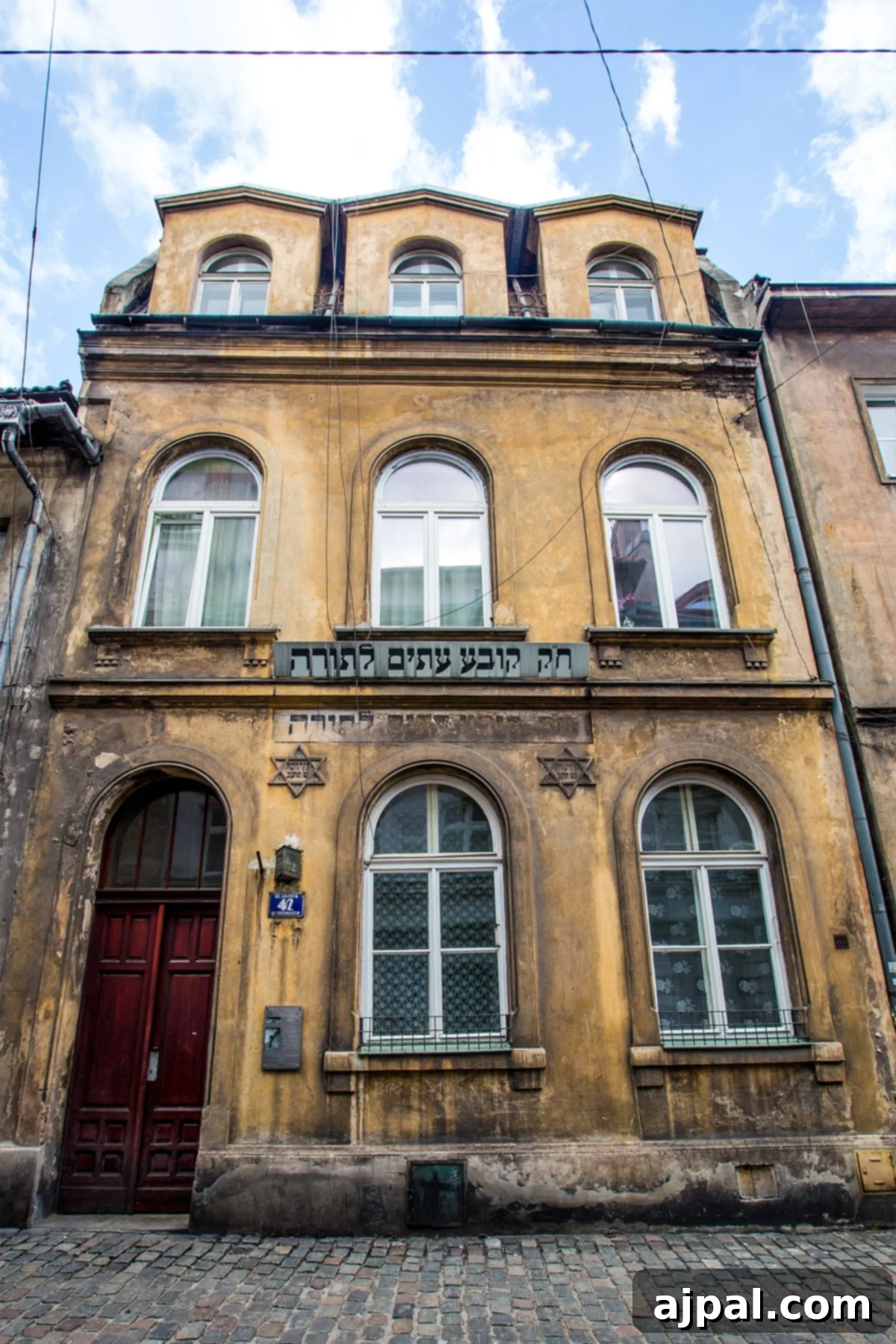An old building with a red door in Kazimierz, Krakow, once a Hebrew School, symbolizing the district's rich history.