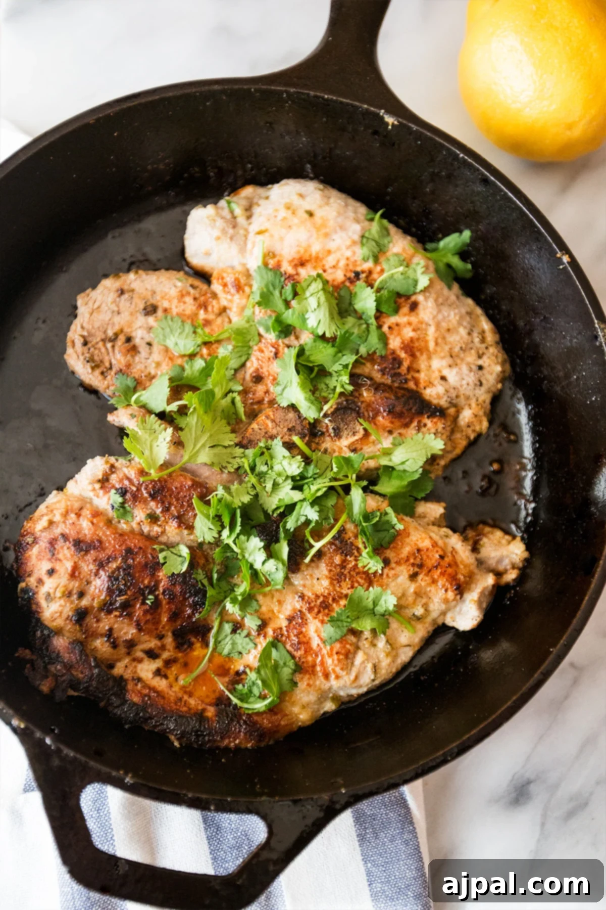 Lemon Garlic Greek Pork Chops 3 Beautifully seared Grecian pork chops, golden brown and garnished with fresh herbs, presented in a cast iron skillet.