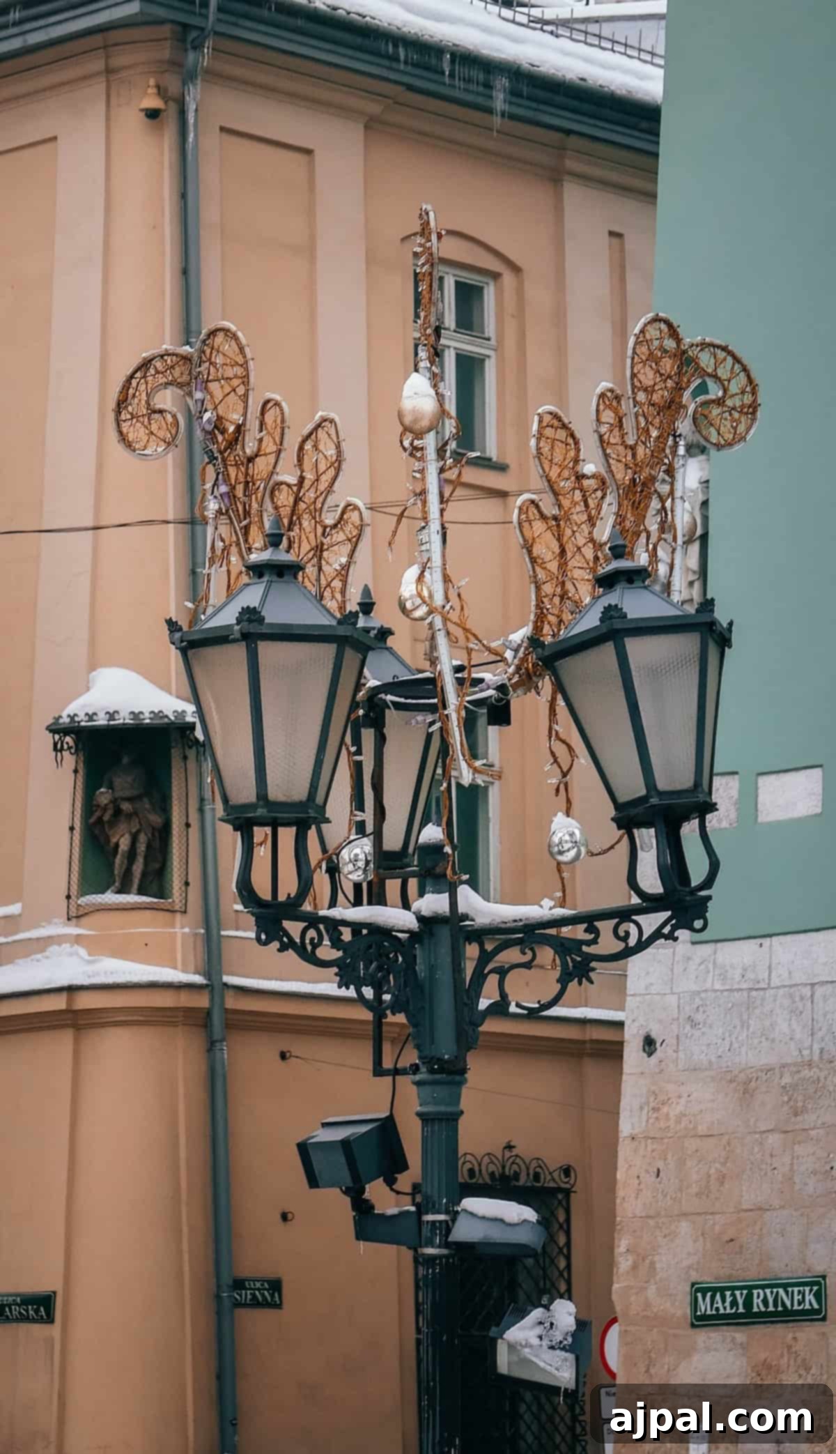 Krakow: Poland's Royal City 14 A vintage street lamp near a peach-colored building on a snowy day in Krakow, with signs indicating "Ma?y Rynek."